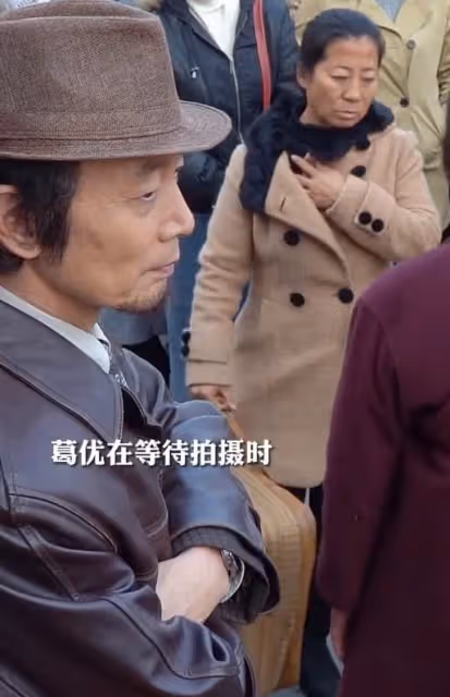 64歲葛優給群演大媽讓座，態度謙和雙手捧上，陪同群演站立等候