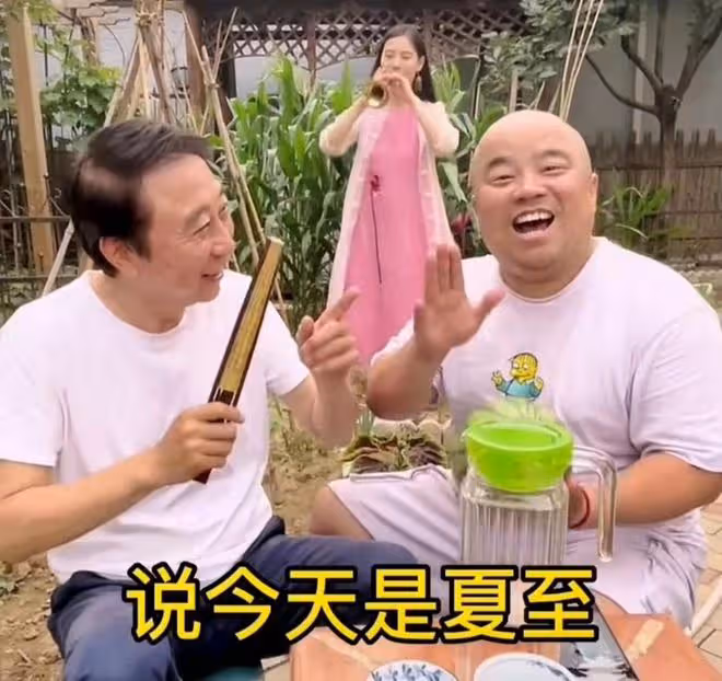馮鞏攜徒弟送夏至祝福,頭髮稀疏眼紋明顯,身後粉衣女吹嗩吶搶鏡