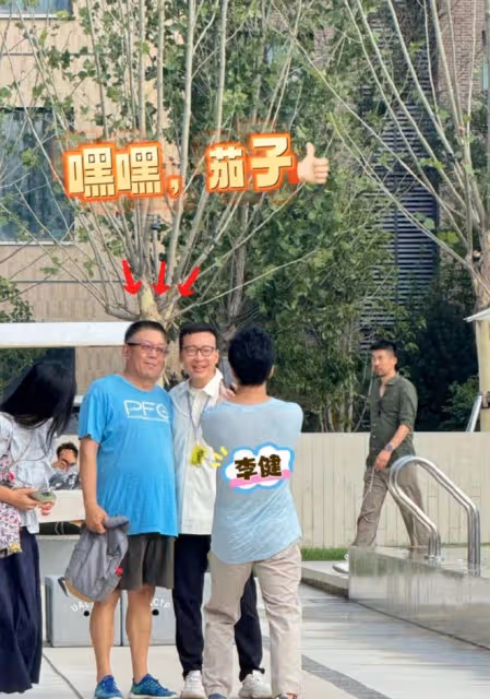 李健幫阿那亞村長拍照,大方端著手機半蹲著,老婆孟小蓓戴著口罩