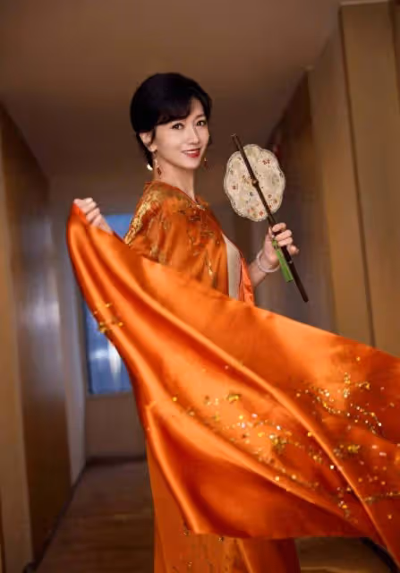 趙雅芝穿橙色長袍雍容華貴，手持團扇似古代仕女
