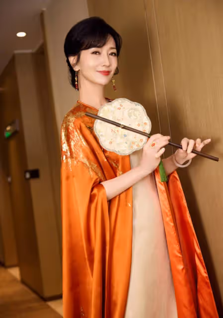 趙雅芝穿橙色長袍雍容華貴，手持團扇似古代仕女
