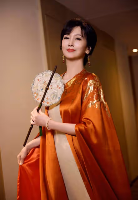 趙雅芝穿橙色長袍雍容華貴，手持團扇似古代仕女